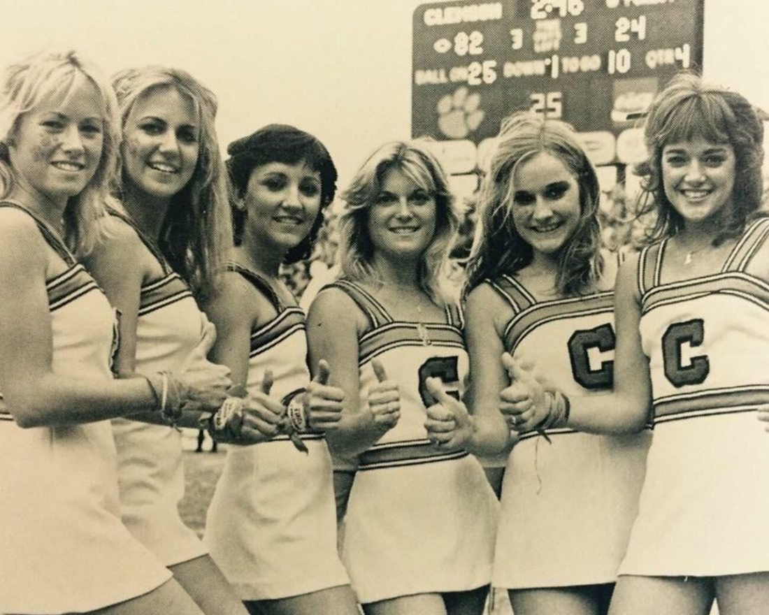 Vintage photo of six Clemson University cheerleaders lined up on game day on football field, smiling at camera with thumbs up. Photo Credits: WIS 10.